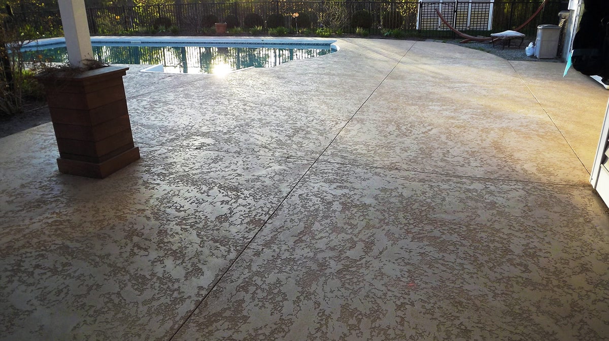 Resurfaced pool deck with polymer concrete overlay and decorative spray topping